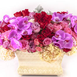 Pink and red roses with purple orchids in a cream vase