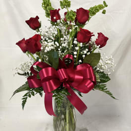 Red roses in a glass vase with baby's breath and a pink ribbon bow