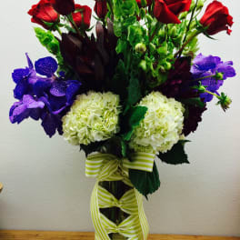 Bouquet of red roses, purple orchids, and white hydrangeas in a glass vase