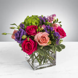 Mixed bouquet of roses, lisianthus, and purple filler in a clear glass cube vase