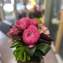 Pink peony bouquet with tropical leaves and small pale blossoms