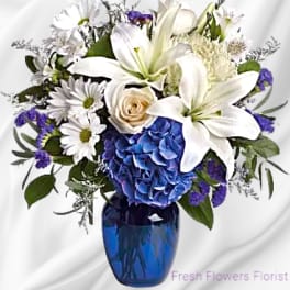 White lilies and daisies with blue hydrangea in a blue vase