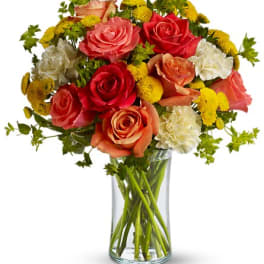 Bouquet of multicolored roses and yellow button flowers in a clear glass vase