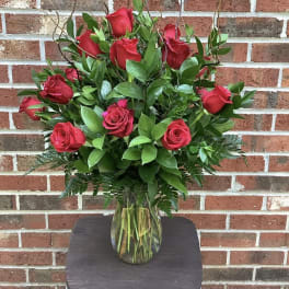 Red roses arranged in a clear glass vase with greenery
