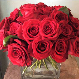 Tight cluster of red roses arranged in a clear square glass vase