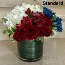 Red roses, white hydrangeas, and blue daisies in a glass vase