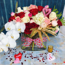 Mixed roses and orchids in a glass vase with heart decorations