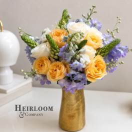 Yellow and white roses with lavender flowers in a gold vase