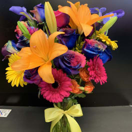 Bright mixed bouquet with orange lilies, dyed roses, and pink daisies in a glass vase