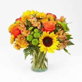 Bouquet of sunflowers, orange roses, and mixed blooms in a glass vase