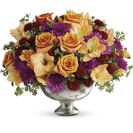 Mixed bouquet of orange roses, purple mums, and peach blooms in a silver pedestal vase