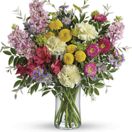 Mixed bouquet of pink, yellow, purple, and white flowers in a glass vase