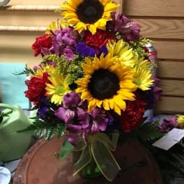 Bouquet with sunflowers, purple alstroemeria, and red carnations in a glass vase