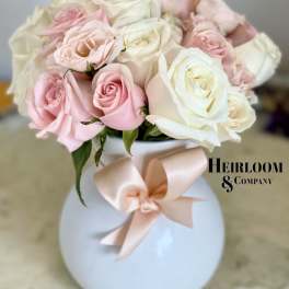 Pink and white roses in a round white vase with a blush ribbon