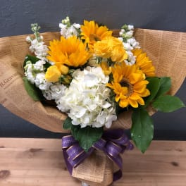 Bouquet of yellow sunflowers, white hydrangeas, and yellow roses wrapped in paper