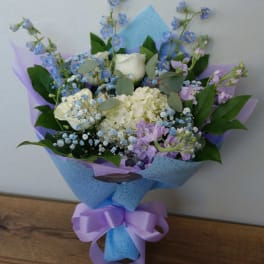 Bouquet of white and lavender flowers wrapped in blue paper with a purple ribbon