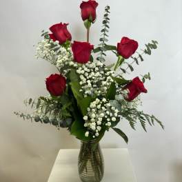 Red roses arranged in a clear glass vase with white filler flowers