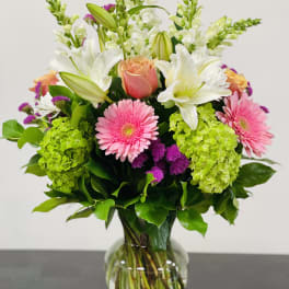 Mixed bouquet with pink gerbera daisies, white lilies, and green hydrangeas in a glass vase