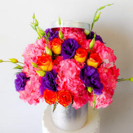 Pink hydrangeas with orange roses and purple blooms in a silver vase