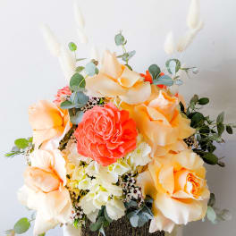Peach and coral roses with white filler flowers in a square container