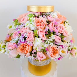 Pink and white floral arrangement in a gold hatbox with a rhinestone band