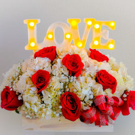 Red roses and white hydrangeas arranged with a lit LOVE sign