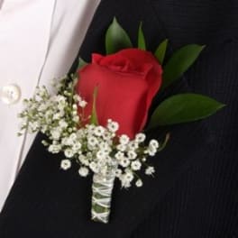 Red rose boutonniere with small white flowers pinned to a black jacket lapel