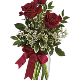Red roses in a clear glass vase with a burgundy ribbon