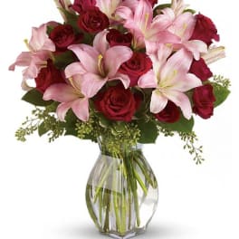 Pink lilies and red roses arranged in a clear glass vase