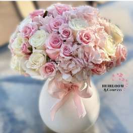 Pink and white rose bouquet in a white vase with a pink ribbon