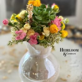 Mixed pink and yellow flowers in a clear glass vase with succulents