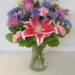 Mixed bouquet of pink lilies, roses, and purple flowers in a clear glass vase