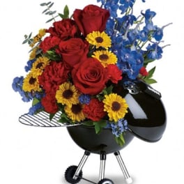 Red roses, yellow daisies, and blue flowers in a black grill-shaped container