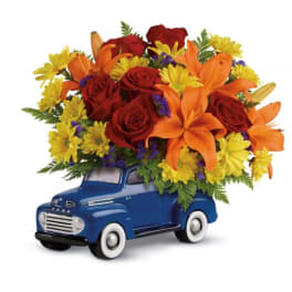 Red roses and orange lilies in a blue toy truck