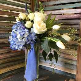Bouquet of white roses and blue hydrangeas in a glass vase with a blue ribbon