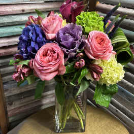Mixed bouquet of pink roses, purple blooms, and hydrangeas in a glass vase