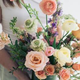 Handheld bouquet of peach, cream, and purple flowers