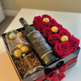 Gift box with red roses, a wine bottle, and a champagne flute with chocolates