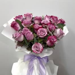 Bouquet of pink roses wrapped in white paper with a lavender ribbon
