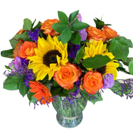 Bouquet of sunflowers, orange roses, and purple filler in a glass vase