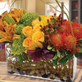 Yellow roses and orange lilies in a glass vase with red blooms