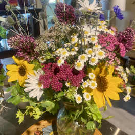 Mixed bouquet with sunflowers, white daisies, and purple allium in a glass vase