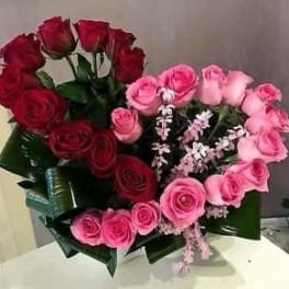 Heart-shaped bouquet of red and pink roses with small white filler flowers