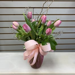 Pink tulips arranged in a vase with a large pink ribbon