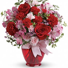 Red roses and pink carnations in a red vase with a pink ribbon