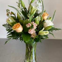 Tall bouquet of peach roses, white lilies, and soft pink flowers in a clear glass vase