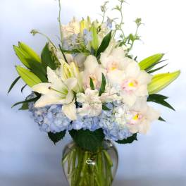 White lilies and orchids in a glass vase with blue hydrangeas