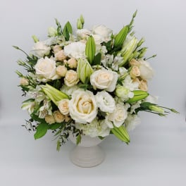 Round arrangement of white and cream roses, lilies, and mixed blooms in a white pedestal vase
