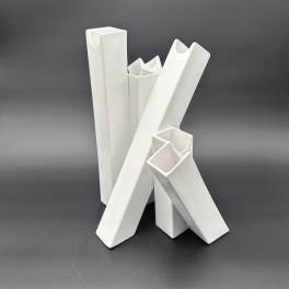 Four white ceramic vases with angular openings on a dark background