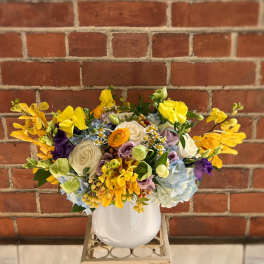 Mixed bouquet of yellow, white, blue, and purple flowers in a white vase